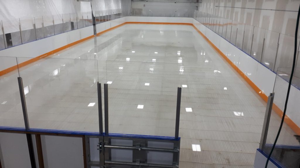 A spacious ice rink featuring a glass wall and a door, inviting skaters to enjoy the smooth surface and bright surroundings.