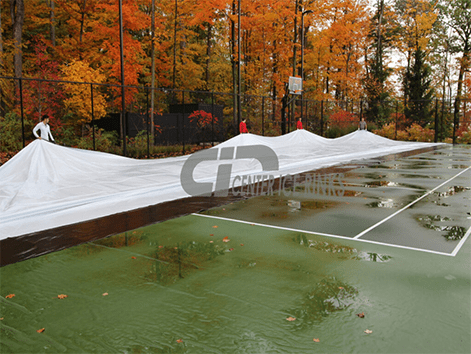A tennis court is completely covered with a blue tarp, protecting the surface from weather elements.