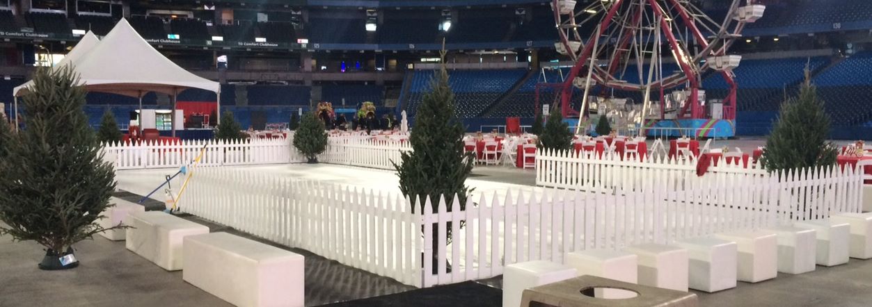 A large white fence surrounds lush trees, with a colorful ferris wheel visible in the background against a clear sky.
